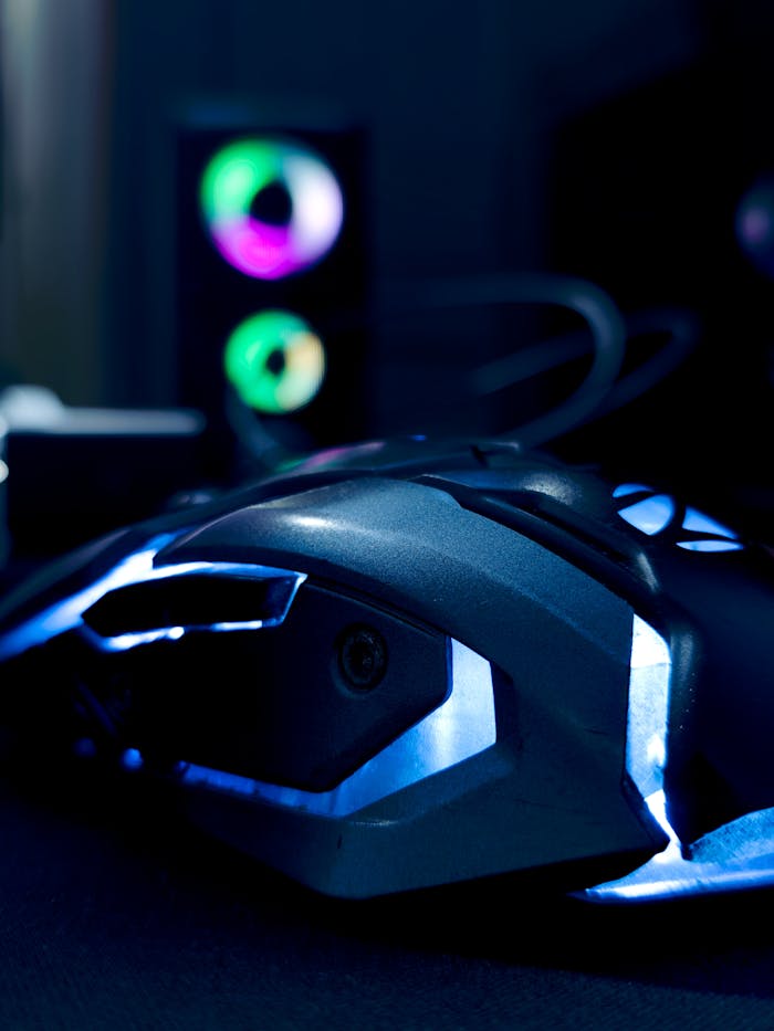 Close-up of a futuristic gaming mouse with RGB lighting and computer setup in a dimly lit room.